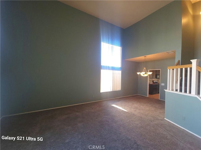 carpeted spare room with a towering ceiling and a chandelier