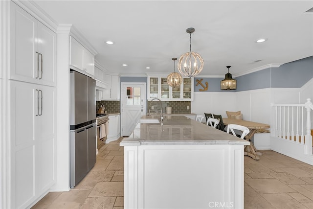 kitchen with crown molding, white cabinetry, backsplash, stainless steel appliances, and a center island with sink