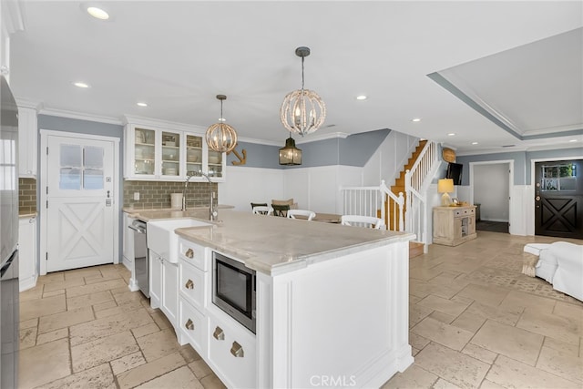 kitchen with appliances with stainless steel finishes, a kitchen island with sink, hanging light fixtures, white cabinets, and decorative backsplash