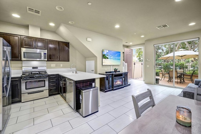 kitchen featuring light tile patterned floors, kitchen peninsula, stainless steel appliances, dark brown cabinetry, and sink