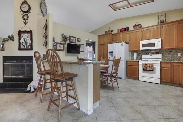 kitchen with backsplash, white appliances, vaulted ceiling, light stone counters, and a breakfast bar