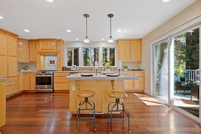 kitchen with a kitchen bar, dark wood-type flooring, an island with sink, light brown cabinetry, and stainless steel gas range oven