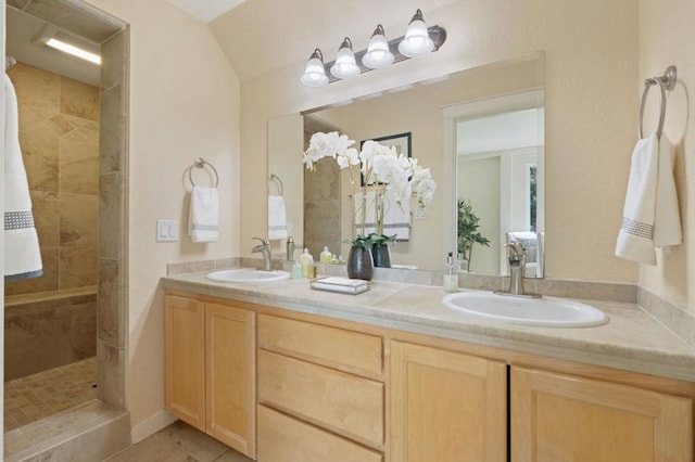 bathroom with vaulted ceiling, vanity, a tile shower, and tile patterned flooring