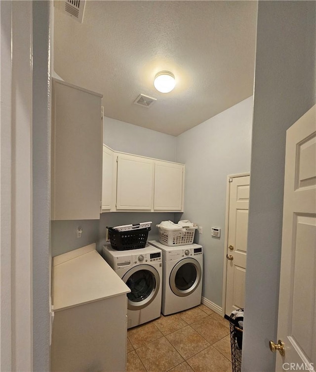 laundry room with washing machine and dryer, cabinets, light tile patterned flooring, and a textured ceiling