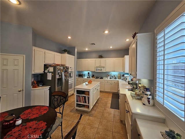 kitchen with stainless steel fridge with ice dispenser, light tile patterned floors, plenty of natural light, white cabinets, and a center island