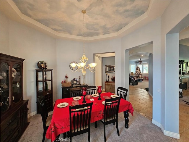 tiled dining area featuring ceiling fan with notable chandelier and a raised ceiling