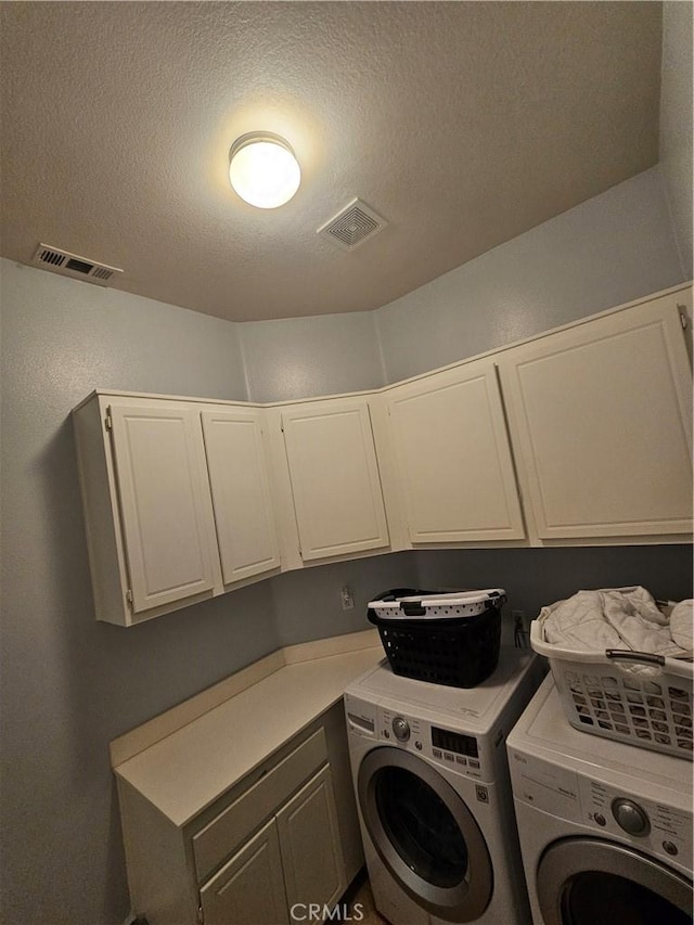 washroom with a textured ceiling, cabinets, and washer and dryer