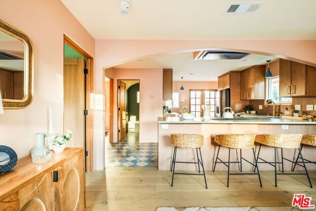 kitchen featuring sink, stainless steel fridge with ice dispenser, kitchen peninsula, light wood-type flooring, and a breakfast bar area