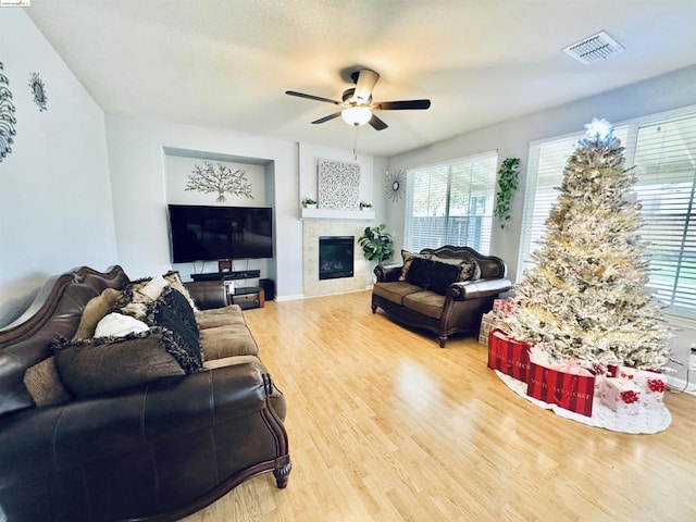 living room featuring ceiling fan, wood-type flooring, and a tiled fireplace