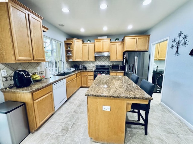 kitchen featuring washer / dryer, a breakfast bar area, appliances with stainless steel finishes, a kitchen island, and sink