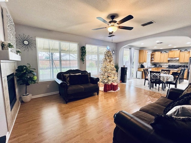 living room with ceiling fan, plenty of natural light, a tile fireplace, and light hardwood / wood-style flooring