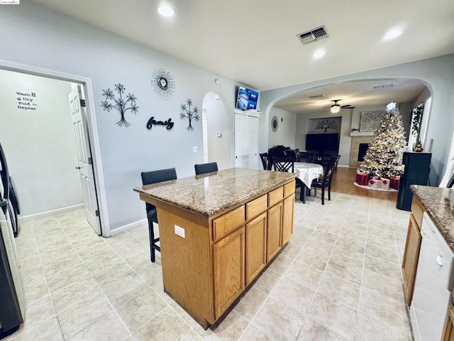 kitchen featuring a kitchen island, ceiling fan, light tile patterned floors, stone counters, and a breakfast bar area