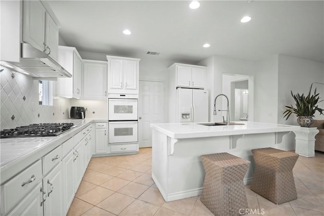 kitchen featuring white appliances, white cabinets, sink, a kitchen breakfast bar, and a center island with sink