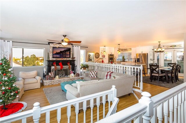 living room featuring ceiling fan with notable chandelier, light hardwood / wood-style flooring, and a fireplace