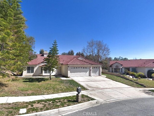 mediterranean / spanish-style house with a tiled roof, concrete driveway, a front yard, stucco siding, and a garage