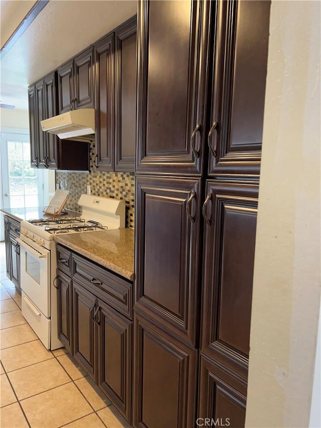 7265 Fletcher View Dr, Highland, CA 92346 - kitchen with white gas range, light tile patterned flooring, under cabinet range hood, backsplash, and dark brown cabinets