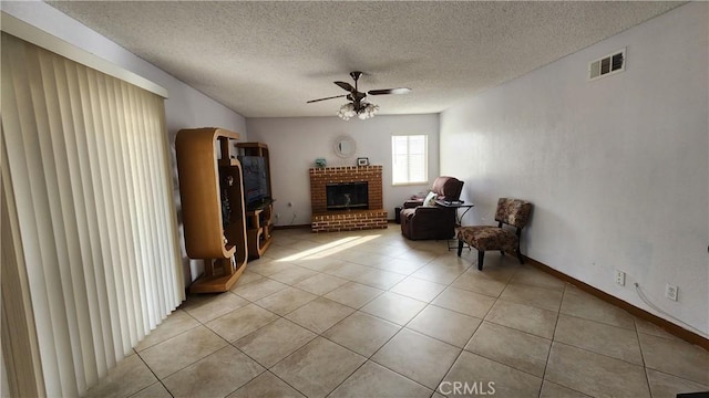 living area featuring ceiling fan, a brick fireplace, light tile patterned flooring, and a textured ceiling