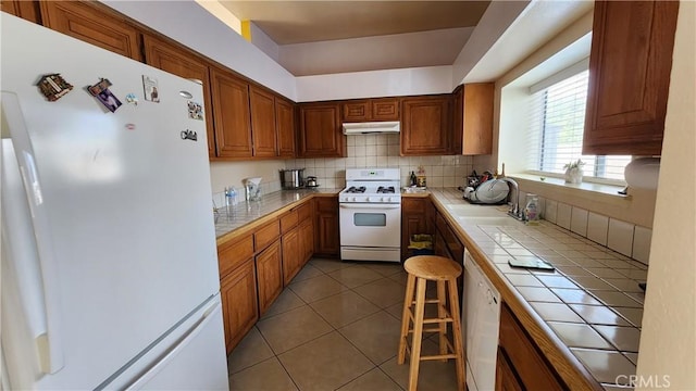 kitchen with tile counters, tasteful backsplash, white appliances, tile patterned floors, and sink