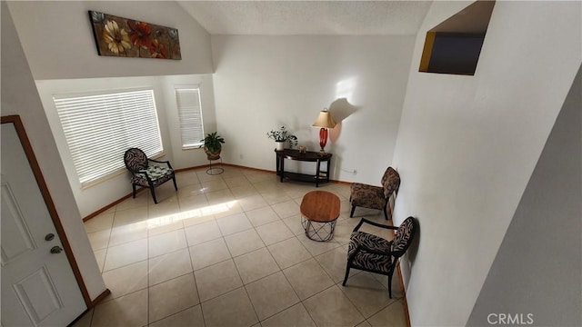 sitting room featuring vaulted ceiling, light tile patterned flooring, and a textured ceiling