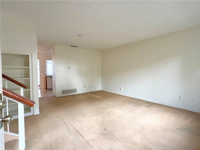 empty room with light colored carpet, built in features, and a textured ceiling