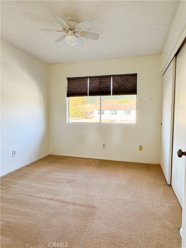 unfurnished bedroom featuring ceiling fan, light colored carpet, a closet, and a textured ceiling