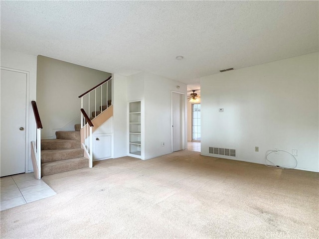 unfurnished living room featuring ceiling fan, a textured ceiling, built in shelves, and light carpet