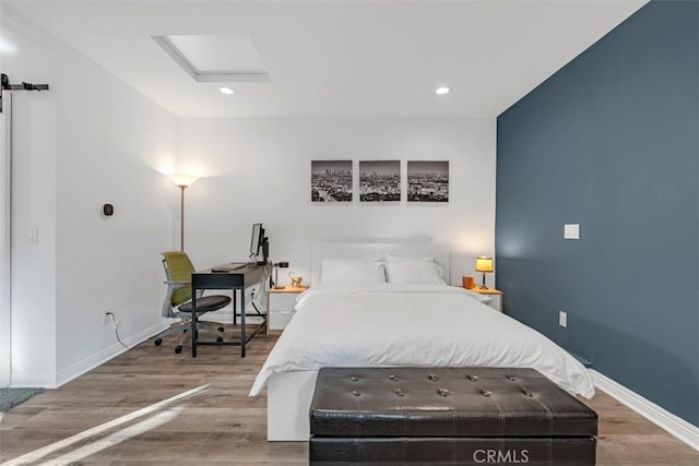 bedroom featuring attic access, a barn door, baseboards, wood finished floors, and recessed lighting