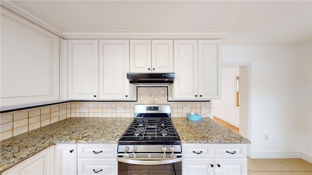 kitchen with tasteful backsplash, under cabinet range hood, light stone counters, and gas range