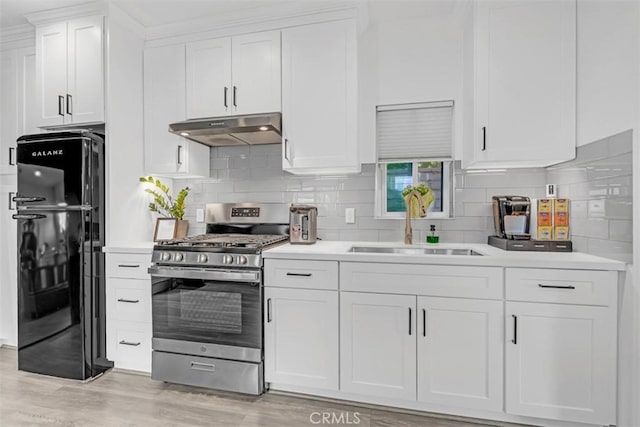 kitchen with stainless steel range with gas stovetop, freestanding refrigerator, light countertops, under cabinet range hood, and a sink