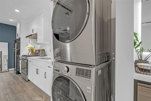 clothes washing area featuring stacked washer and dryer, recessed lighting, laundry area, and light wood-style flooring