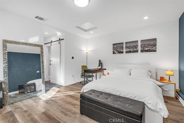 bedroom with a barn door, wood finished floors, visible vents, and recessed lighting