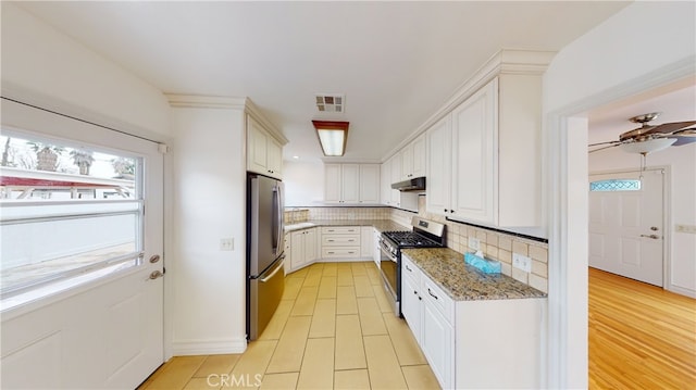 kitchen with stainless steel appliances, under cabinet range hood, light stone counters, and tasteful backsplash