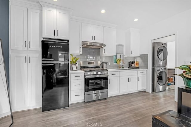 kitchen with freestanding refrigerator, stainless steel gas stove, a sink, stacked washing maching and dryer, and under cabinet range hood