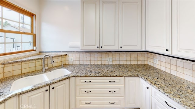 kitchen featuring light stone countertops, white cabinetry, backsplash, and a sink