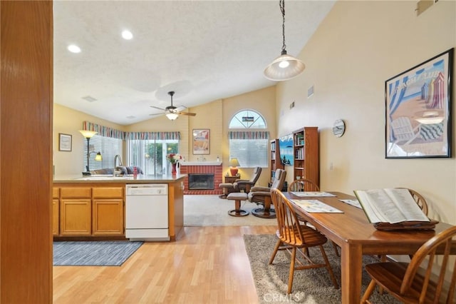 kitchen featuring dishwasher, decorative light fixtures, sink, light hardwood / wood-style floors, and lofted ceiling