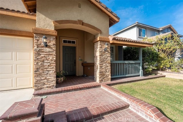 view of exterior entry featuring covered porch, a garage, and a lawn