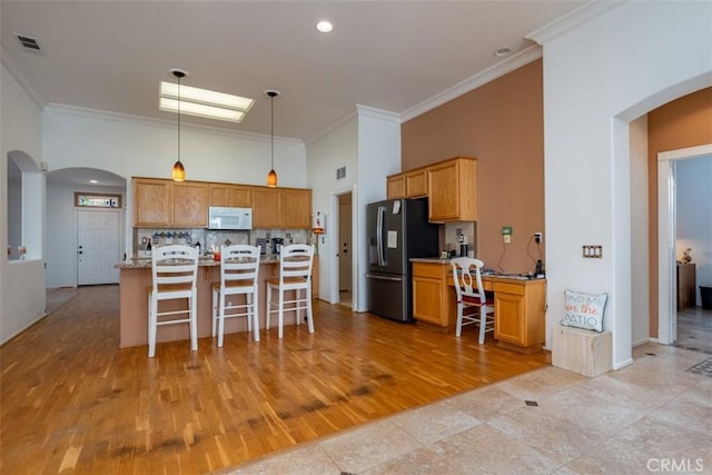 kitchen featuring stainless steel refrigerator with ice dispenser, decorative light fixtures, light stone counters, and ornamental molding