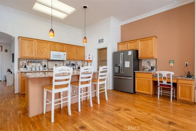 kitchen featuring pendant lighting, tasteful backsplash, stainless steel fridge, crown molding, and a breakfast bar area