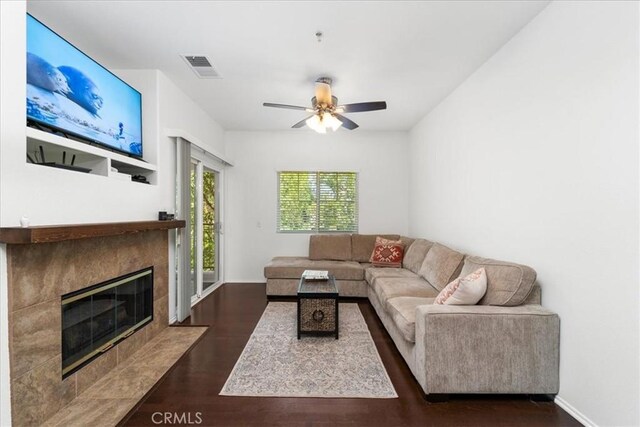 living room with ceiling fan, a fireplace, and dark wood-type flooring