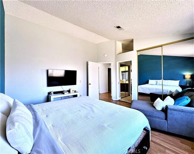 bedroom with lofted ceiling, a textured ceiling, a closet, and wood-type flooring