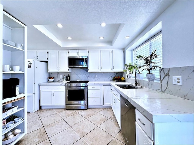 kitchen featuring appliances with stainless steel finishes, white cabinets, sink, and a tray ceiling