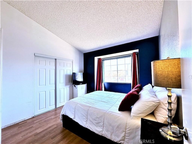 bedroom featuring a closet, hardwood / wood-style flooring, a textured ceiling, and vaulted ceiling