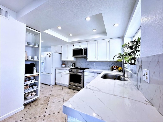 kitchen with appliances with stainless steel finishes, light stone countertops, a tray ceiling, sink, and white cabinetry