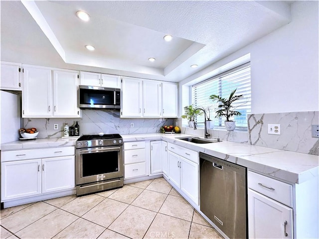 kitchen with sink, a raised ceiling, appliances with stainless steel finishes, and white cabinetry