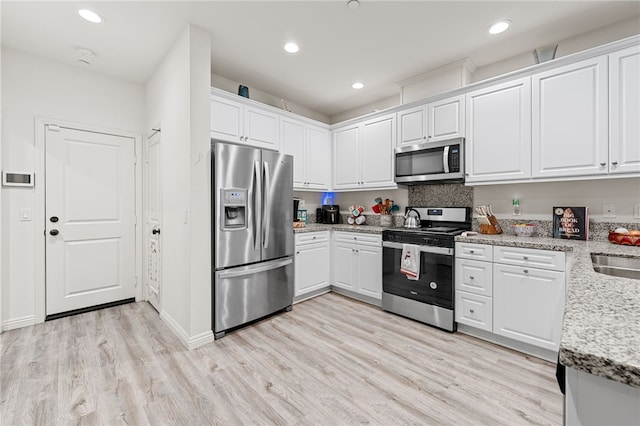 kitchen with sink, appliances with stainless steel finishes, white cabinetry, light stone counters, and light hardwood / wood-style floors