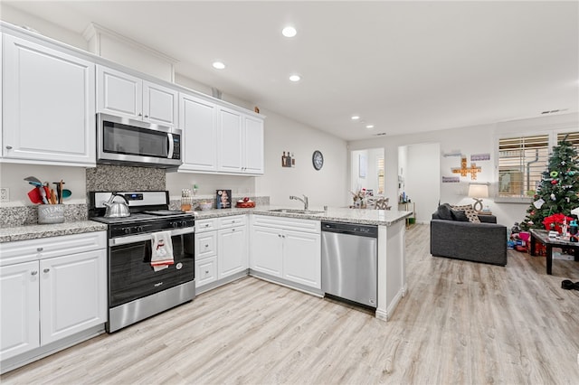 kitchen featuring appliances with stainless steel finishes, white cabinets, a sink, light wood-type flooring, and a peninsula