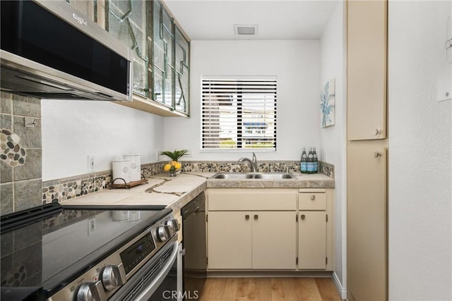 kitchen featuring appliances with stainless steel finishes, decorative backsplash, light wood-type flooring, cream cabinets, and sink