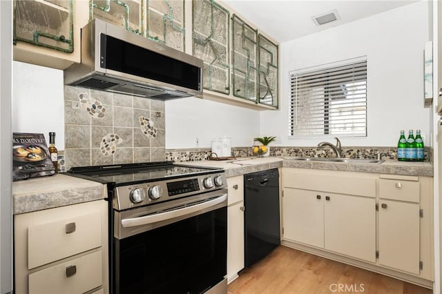 kitchen featuring tasteful backsplash, light wood-style flooring, appliances with stainless steel finishes, light countertops, and a sink