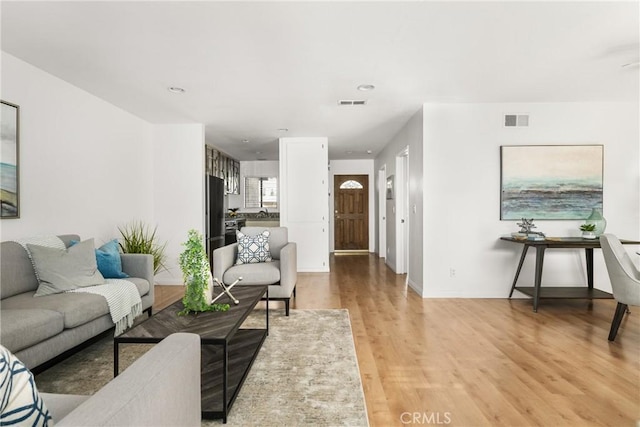 living room with light wood finished floors, baseboards, and visible vents