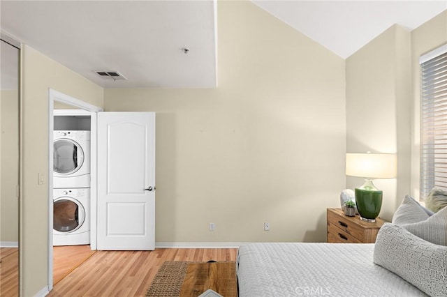 bedroom featuring stacked washing maching and dryer and light hardwood / wood-style floors